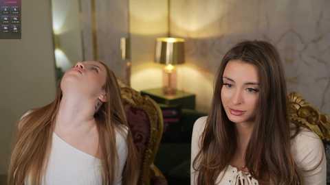 Video of a fair-skinned woman with long brown hair, wearing a beige top, leaning back with eyes closed in a sultry pose. Background includes a gold lamp, dark furniture, and ornate wallpaper.