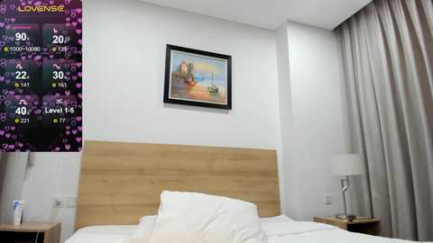 Video of a minimalist, modern hotel room with a wooden headboard, white bedding, a framed painting, and a digital clock displaying 20\u00b0C.