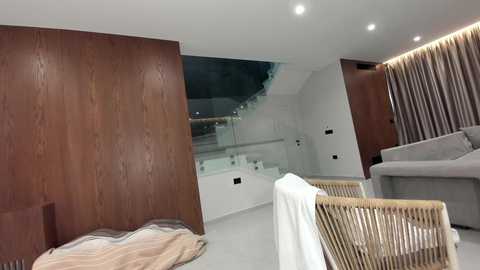 Video of a minimalist living room with dark wood paneling, glass railing, modern gray sofa, white floor, and striped rug.