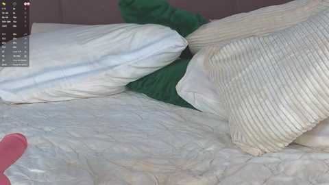 A video of a messy bed with crumpled white sheets, a green pillow, and a beige blanket, all on a pink mattress, with a digital interface overlay showing time and temperature.