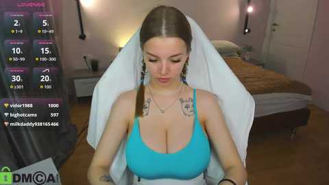 Video of a fair-skinned woman with light brown hair, wearing a blue bra and white veil, in a bedroom.