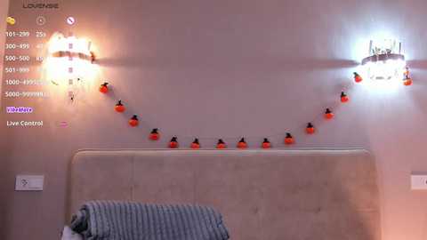 Video of a cozy bedroom with a beige tufted headboard, two wall-mounted sconces with orange lightbulbs, and a string of pumpkin lights above.