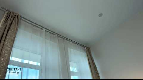 Video of a minimalist, modern bedroom featuring large, sheer white curtains framing a window with multiple panes, letting in soft daylight. The ceiling is plain white, with a small recessed light fixture in the center. Text \"ONLYFANS: @taihroomporn\" is visible in the bottom left corner.