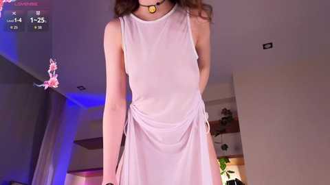 Video of a slender, fair-skinned woman with long, wavy brown hair, wearing a sheer, light pink, sleeveless dress, standing in a modern, dimly-lit living room with purple lighting, shelves, and potted plants.