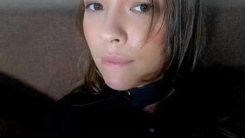 Media: Video of a young woman with fair skin, light brown hair, and brown eyes, wearing a black leather jacket and a black choker. She has a neutral expression, looking to the right.