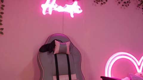 Video of a pink room with a large guitar-shaped couch, pink neon lights, and a black pillow on the couch, creating a playful, retro aesthetic.