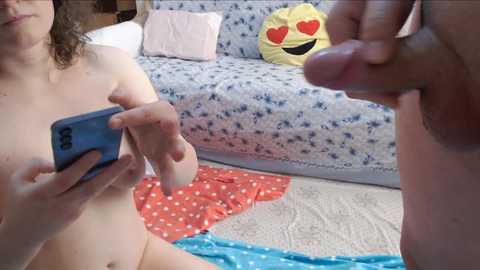 Media: A video shows a naked man with an erect penis, holding a blue phone, and a naked woman with curly hair, in a room with a bed and a yellow Pac-Man pillow.