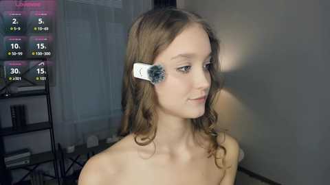 Media: Video of a young, fair-skinned girl with wavy brown hair, wearing a white headband with a black sensor, standing indoors.