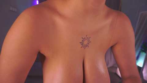 Video of a topless woman with light skin, showcasing a sun tattoo on her chest and a glimpse of her breasts. Background features blurred indoor elements, including a purple light.