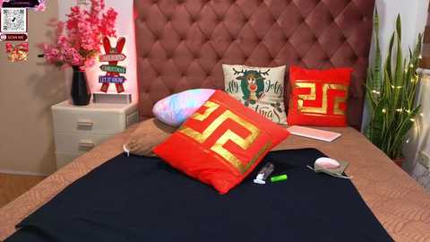 A video of a modern bedroom with a tufted pink headboard, pink floral wall decor, and decorative pillows featuring Chinese characters and greenery.