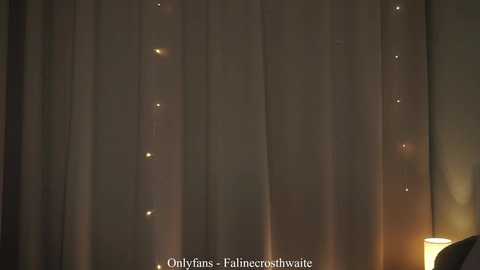 Video of a dimly lit room featuring a sheer curtain with small, scattered lights creating a soft, ambient glow. The background is dark, and a small portion of a bedside lamp is visible on the right. Text at the bottom reads \"Onlyfans.com/filncerustwinkle.\