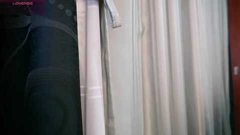 A video of a dark green velvet curtain with a white sheer overlay, positioned in a dimly lit room. The curtains have subtle, horizontal white stripes. The image includes a watermark reading \"LOVEBOMBING.\