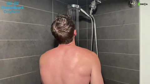 Video of a shirtless, muscular man with short brown hair showering in a modern, gray-tiled shower. Water flows from a handheld showerhead. Text in the upper left reads, \"The Daily Mail Online.\