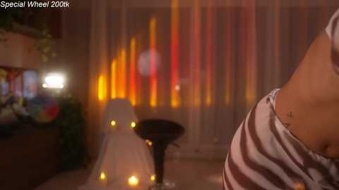 A video showing a person with a tattoo, wearing a striped shirt, standing near a lit candle in a dimly-lit room with a wall of colorful vertical lights.