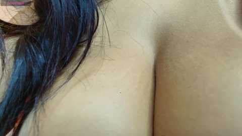 Video of a woman's bare back, showing light skin and dark blue hair. The image is close-up, focusing on the skin texture and hair.