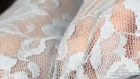Video of a close-up, textured white lace fabric with a delicate, floral pattern, subtly revealing skin tones underneath. The image captures intricate lacework and soft, blurred background.