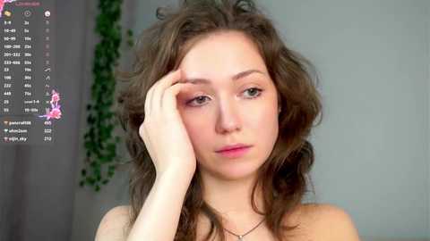 Media: Video of a young woman with wavy brown hair, light skin, and pink lips, wearing a strapless top, against a green-leafed background, with a calendar app visible.