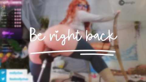 Video of a busty, curvy, red-haired woman in glasses, wearing glasses, bending over a chair in a brightly lit room, with \"Be right back\" text overlay.