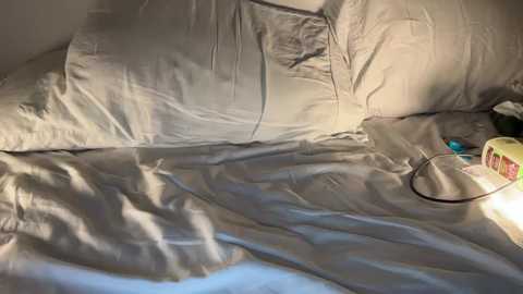 A video of a neatly made bed with light gray sheets and pillows, a yellow toy, and a power cord on the side, suggesting a cozy, everyday domestic scene.