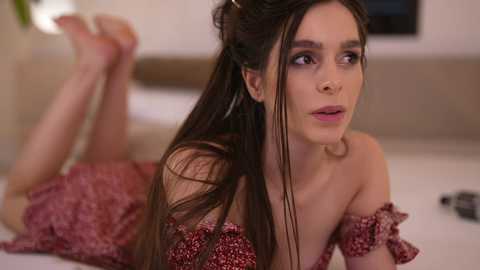 Media: Video of a young woman with long dark hair lying on her stomach in a red floral dress, with a blurred background showing a modern living room.
