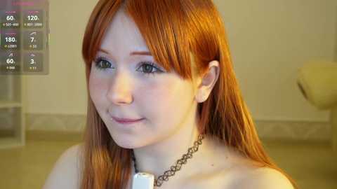 Video of a fair-skinned woman with long, straight red hair, light makeup, wearing a black choker necklace. She's indoors, smiling slightly, with a blurred background.