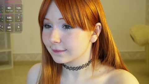 A video of a young woman with long, straight red hair and pale skin, wearing a black choker necklace, set indoors with a cream-colored wall and a beige floor.