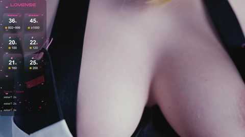 A close-up video of a fair-skinned woman's bare breast, partially obscured by a black bra strap, with a smartphone displaying a weather app in the background.