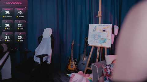 Video of a colorful, cluttered room with a guitar, painting on an easel, and a woman's hand visible, against blue curtains.