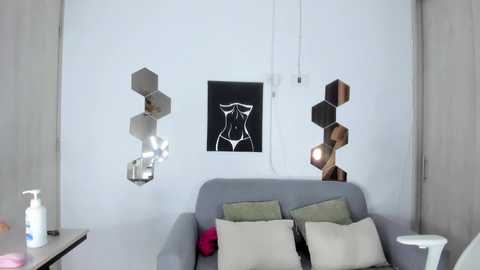 Video of a minimalist, modern living room featuring a grey sofa with green and white pillows, hexagonal wall art, and a sleek, metallic floor lamp.