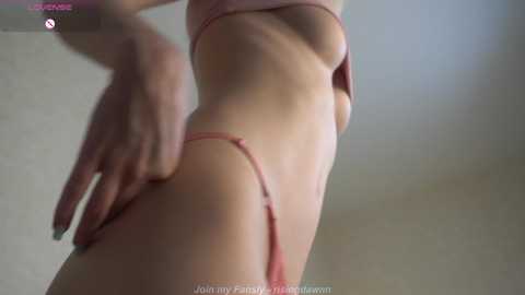 Video of a light-skinned, slender woman in pink lingerie, viewed from the side, highlighting her small breasts and curvy hips.