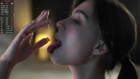 Media: Video of a fair-skinned woman with brown hair, licking a drop of water from her finger, set against a dimly lit, blurred background.