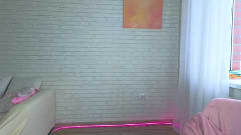 Video of a minimalist bedroom with white brick wall, light pink rug, pink neon lights, and a pink chair.