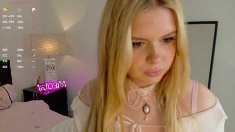 Video of a blonde woman with fair skin, wearing a white lace top, in a modern bedroom with a white lamp, black nightstand, and \"WORDBOMB\" overlay.