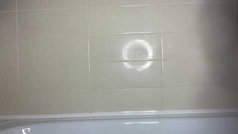 A video of a bathroom wall with white tiles, showing a circular water stain in the middle of the tiled area. The lower part of the image shows the edge of a white bathtub.
