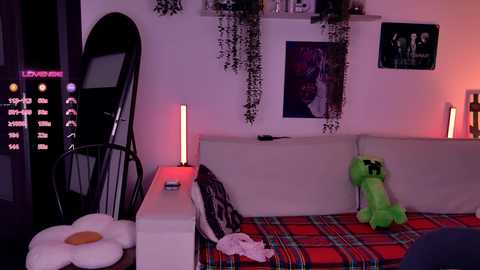 Video of a dimly-lit, modern living room with a beige couch, red and green plush toys, and purple wall decor, featuring a large, black mirror and a digital clock.