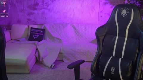 Video of a gaming setup featuring a black gaming chair with white accents, a beige sectional couch with a blanket, and a purple lighted background.