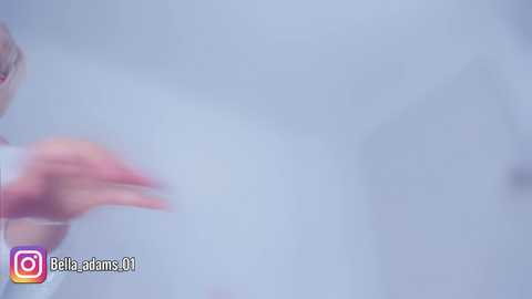 Video of a blurred, light-skinned person with long, pink-painted nails, wearing a white top, against a pale, misty background. The image has a soft focus and is marked with a Bellaire Fans logo.