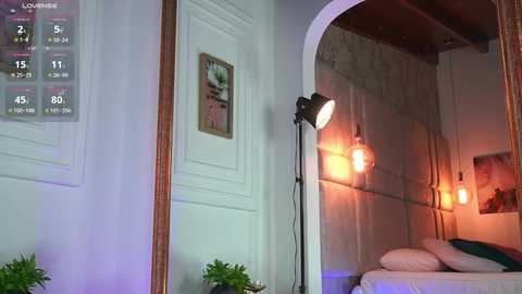 Video of a cozy bedroom with a bed, white walls, framed artwork, a large mirror, and hanging pendant lights; a digital clock shows 4:58 AM.