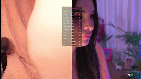 A close-up video of a woman with long black hair, wearing a light peach robe, partially obscured by a calendar overlay, in a dimly lit room with potted plants and curtains.