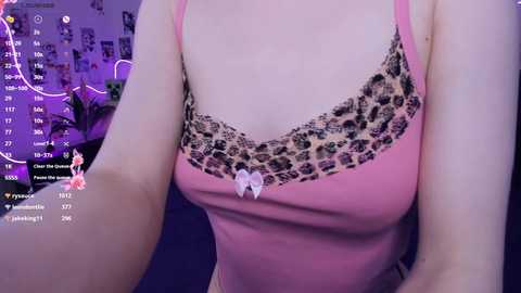 Video of a pale-skinned woman in a pink camisole with leopard print lace trim and a small bow, seen from the chest up, with a purple background.