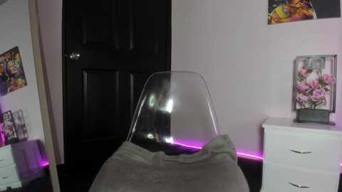 Video of a modern, minimalist bedroom with a clear acrylic chair, a white dresser, a black door, and vibrant floral artwork on the walls.