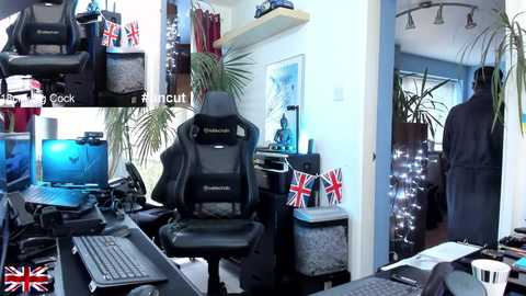 Video of a modern, cluttered gaming room with a black gaming chair, multiple computer screens, a Union Jack flag, and a man in a robe walking out.
