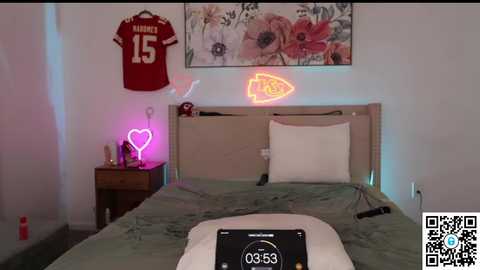 Video of a bedroom with a green bedspread, a neon heart, a football jersey, a fishbowl, and a QR code.
