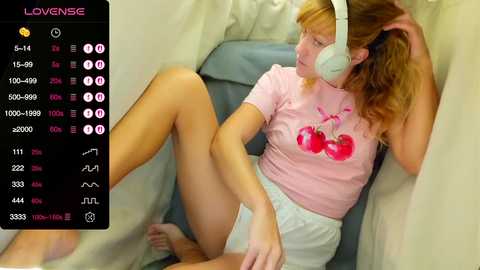 Video of a young woman with blonde hair, wearing a pink T-shirt and white shorts, lying on a bed with headphones, surrounded by a digital interface displaying music controls.
