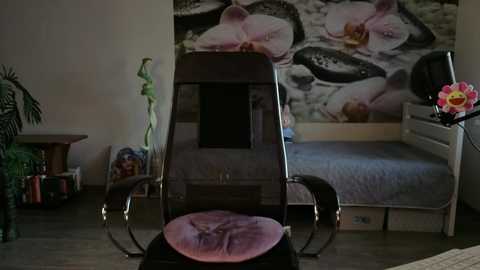 Video of a dimly lit bedroom with a dark wooden chair and floral wallpaper, featuring a bed with a pink cushion, and a pink flower vase.