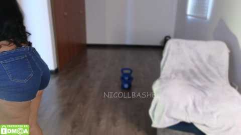 Video of a woman's backside in denim shorts and a man's leg, with a blue dildo on a wooden floor.