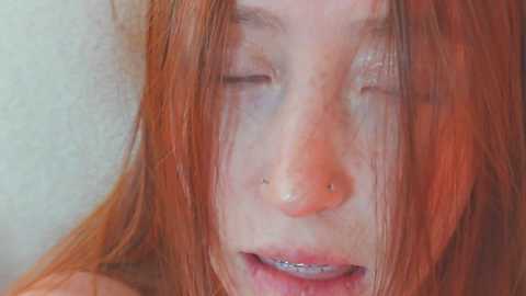 Video of a young woman with fair skin, long red hair, and silver braces, wearing a nose ring, eyes closed, and smiling.