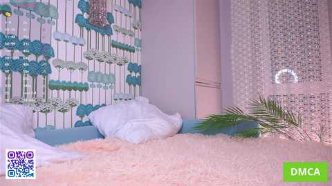Video of a whimsical bedroom featuring a white bed with fluffy pillows, pastel walls adorned with a colorful floral wallpaper, a light pink shag rug, and a silver beaded curtain.