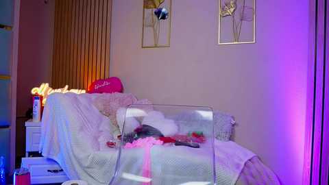 Video of a cozy, pink-themed bedroom with a white crib covered in plush toys, framed art, and soft lighting.