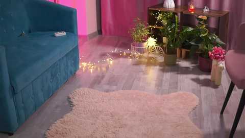 Video of a cozy, vibrant living room with a blue sofa, green plants, pink walls, wooden floor, and a fluffy white rug.